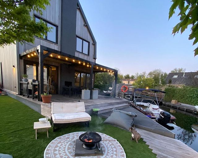 Moderne zwarte houten pergola met sfeerverlichting aan een woning bij het water. Stijlvolle overkapping zonwering. pergola koppelstukken rijpex